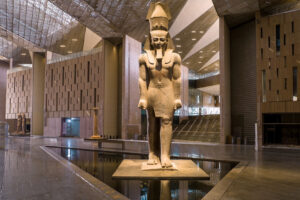 The colossal standing statue of Ramses II inside the grand glass-roofed atrium of the Grand Egyptian Museum in Giza.