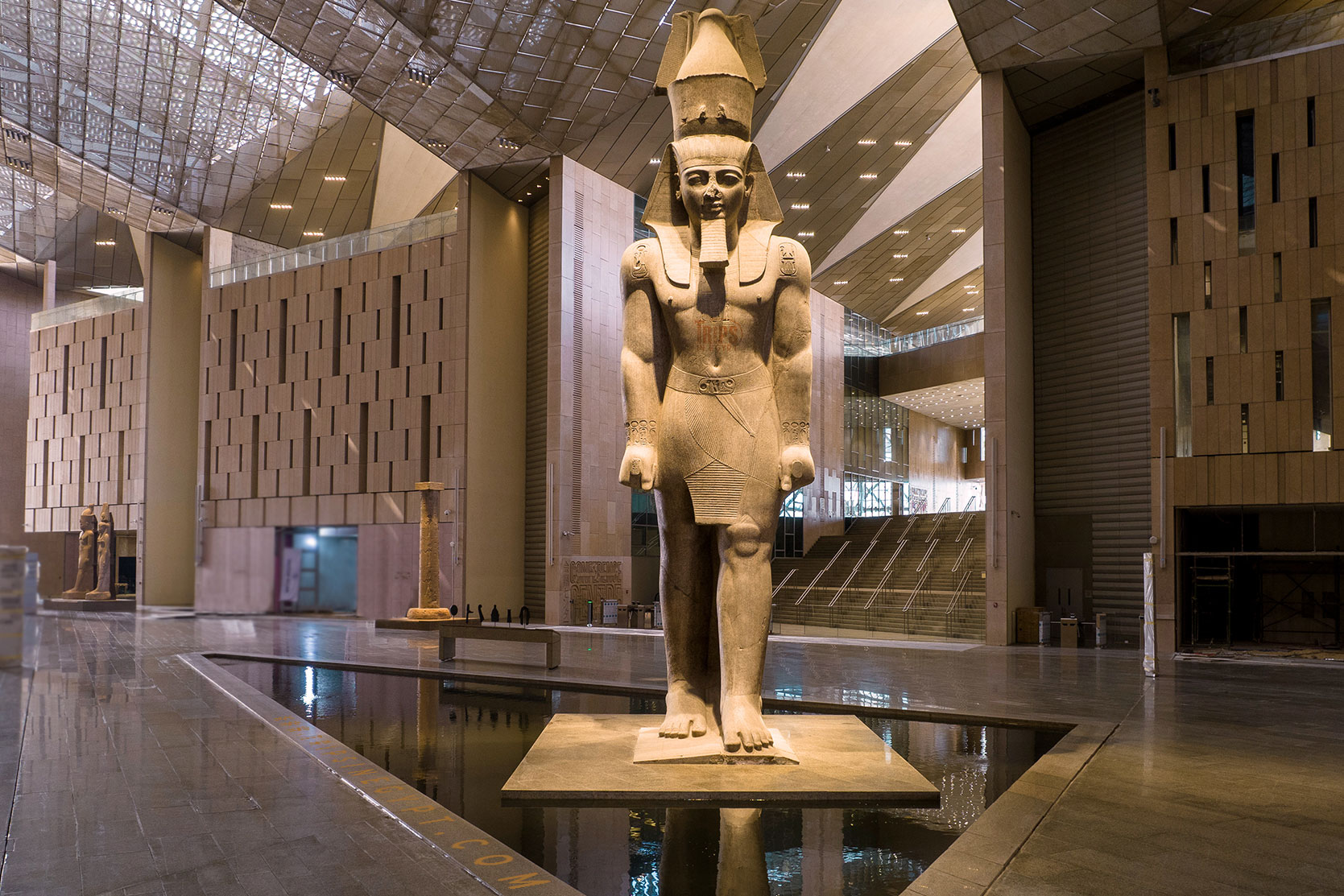 The colossal standing statue of Ramses II inside the grand glass-roofed atrium of the Grand Egyptian Museum in Giza.