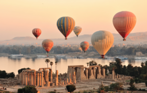 Colorful hot air balloons flying over the Nile River and ancient temple ruins in Luxor during a sunrise flight.